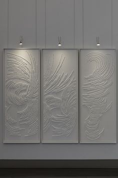 three white paintings hanging on the side of a wall