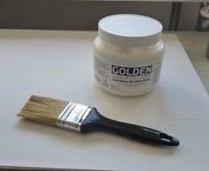 a paint brush sitting on top of a table next to a jar of white paint