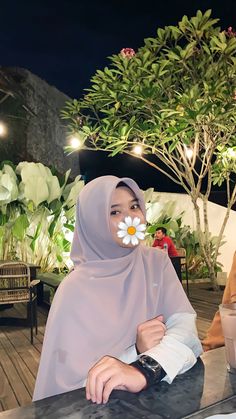 a woman in a hijab sitting at a table with a flower on her nose