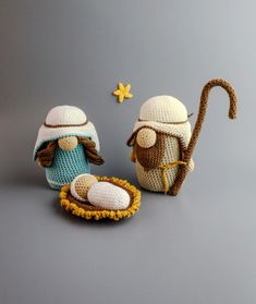 two crocheted nativity items are displayed on a gray surface, one is wearing a hat and the other has a cane