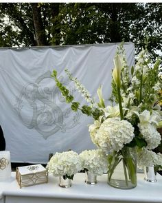 white flowers are in vases and candles on a table with a banner behind them