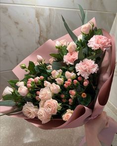 a bouquet of pink and white flowers on a marble counter top with greenery in the corner