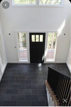 an overhead view of a black door and stairs in a white room with two windows