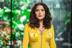 a woman in a yellow dress standing next to a green wall with plants on it