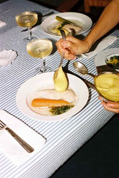 a person is spooning food from a plate on a table with wine glasses and utensils