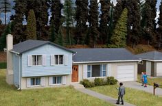 two children are standing in front of a blue house with trees on the hill behind them