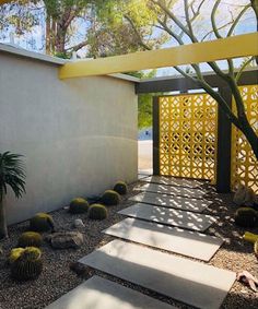 an outdoor area with rocks, cactus and yellow trellis on the side of it