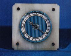 a clock with roman numerals on it sitting on a blue cloth covered surface