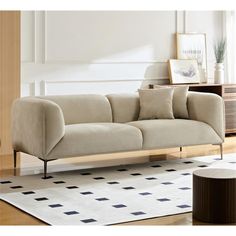 a beige couch sitting on top of a wooden floor next to a white rug and table