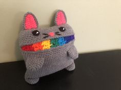 a crocheted stuffed animal with a rainbow in its mouth sitting on a table