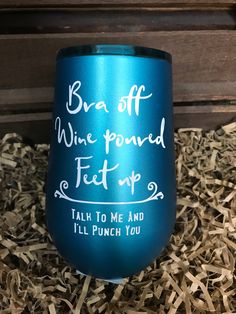 a teal colored wine cup with white writing on it in some wood shavings