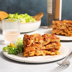 two plates with lasagna casserole on them and salad in the background