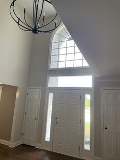 an empty room with three doors and a chandelier hanging from the ceiling in front of two windows