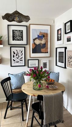 a dining room table with chairs and pictures on the wall above it, along with vases filled with flowers