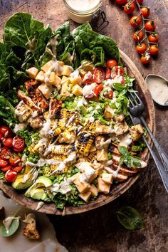 a salad with chicken, lettuce and tomatoes in a wooden bowl on a table