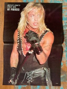 a man with long blonde hair wearing leather gloves and holding a knife in his right hand