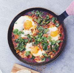 an iron skillet with eggs and greens on it next to bread, knife and napkin