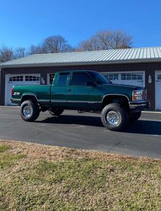 a green pick up truck parked in front of a garage