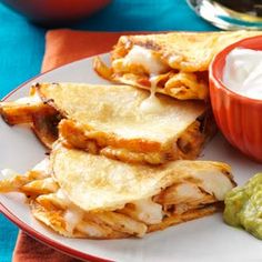 a plate topped with quesadillas and guacamole next to a bowl of sour cream