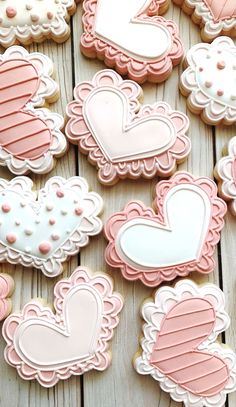 decorated cookies with pink and white icing are arranged on a wooden surface, including hearts