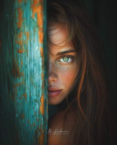 a woman with blue eyes peeking out from behind a wooden door