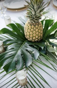 a pineapple sits on top of a green leafy table runner with place settings