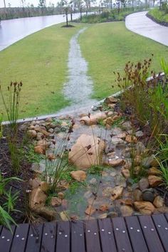 a small stream running through a lush green field next to a wooden walkway with rocks and grass