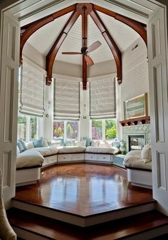 an open living room with wooden floors and white furniture in the center, surrounded by large windows