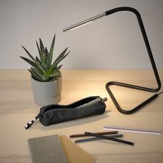 a desk with a lamp, pencils and an open book on it next to a potted plant