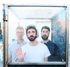 three men standing in front of a window with their hands up to the camera,