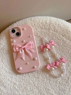 a pink phone case with pearls and bows on it next to a pair of earrings