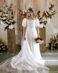 a woman wearing a white dress standing in front of flowers