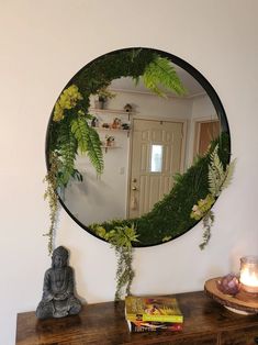 a mirror that is on the wall above a table with a candle and some plants