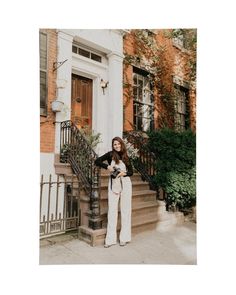 a woman standing in front of a brick building with stairs and potted plants on either side