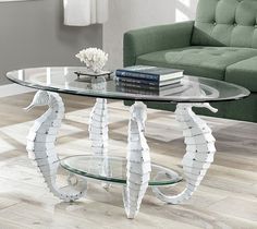 a glass coffee table with white seahorses on the top and bottom, sitting in front of a green couch