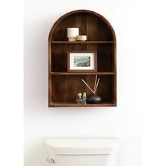 a wooden shelf above a toilet in a white bathroom with pictures and candles on it