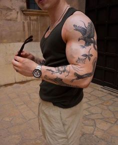 a man with tattoos on his arm holding an umbrella and looking at the camera while standing in front of a building