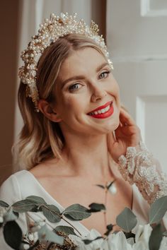 a woman wearing a tiara with flowers and greenery around her neck smiling at the camera