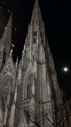 an old cathedral lit up at night with the moon in the background