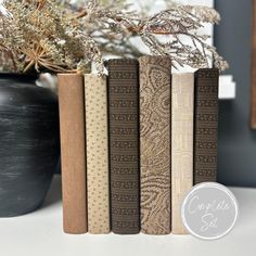 four books sitting on top of a white table next to a potted plant in a black vase