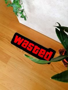 a red and black sticker sitting on top of a wooden floor next to a potted plant