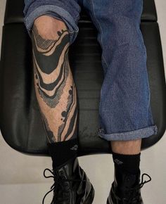 a man sitting on top of a black chair with his legs crossed and tattoos on the leg