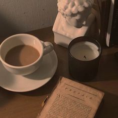 a cup of coffee sitting on top of a table next to an old book and candle