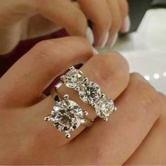 a woman's hand holding two rings with three diamonds on top of each one