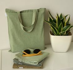 a green tote bag sitting on top of a white table next to a potted plant