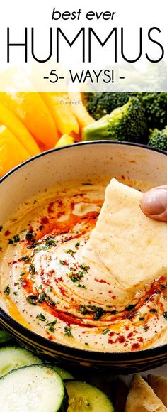 a hand dipping hummus into a bowl with cucumbers