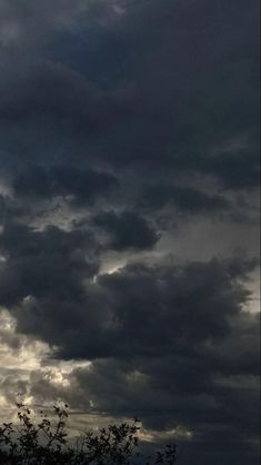 an airplane is flying in the sky with dark clouds behind it and some trees below