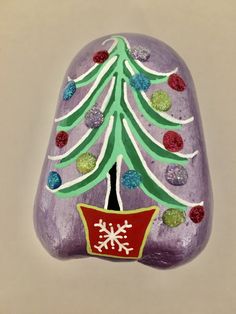 a purple rock with a christmas tree painted on it and snowflakes around the top