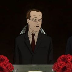 two men sitting at a table with roses in front of them and one man wearing glasses