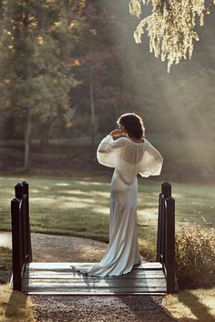 a woman in a white dress is standing on a bridge and looking at the trees